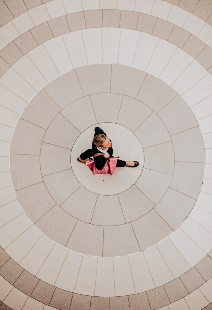 Overhead photo of well-dressed woman full-stride at the center of a mandala of stone tiles.